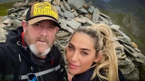 Tim Edwards, wearing a baseball cap, poses for a photograph with his blonde-haired daughter Elle. They are standing at the top of Mount Snowdon. 