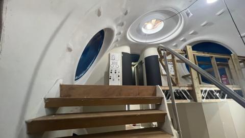 Inside the wooden prototype of a capsule set to go underwater. Stairs and communal area.