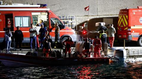 Emergency and rescue service officials work at a port near the site where a luxury yacht sank