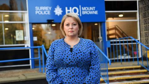 Surrey PCC Lisa Townsend - a woman with short blonde hair stands outside Surrey Police's HQ with a black and blue dress on