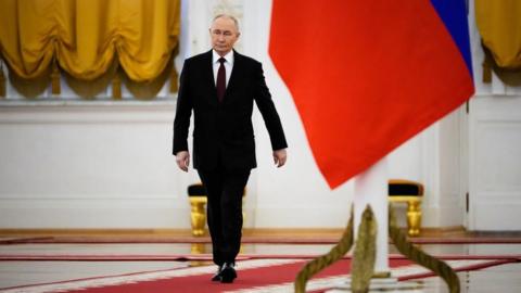 Vladimir Putin walking past a Russian flag in the Kremlin
