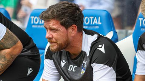 Darrell Clarke leaning forward with his arms on his knees while sat in the dugout 