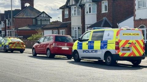 A police van and a police car parked on a street. A red Vauxhall is parked between them.