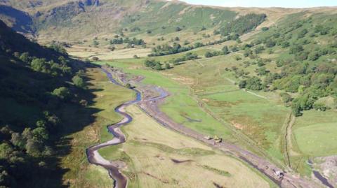 An aerial view of two streams of water down a rural valley. Diggers are working on one stream, the other meanders through the fields.