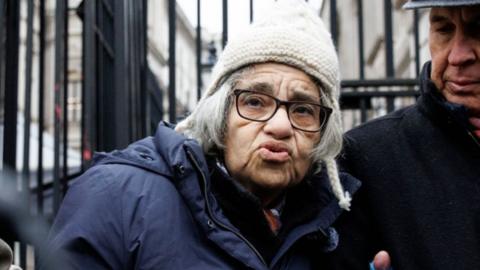 Laila Soueif, an elderly woman, is supported by two people either side of her as she gives a statement to the members of media outside the gates of Downing Street.