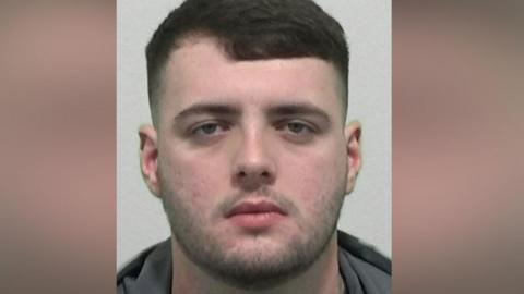 Mugshot of Harry Farrer. He has faint dark stubble and neat short dark hair.