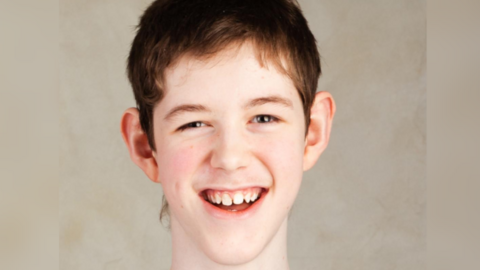 A teenage boy with short brown hair, smiling and looking directly at the camera