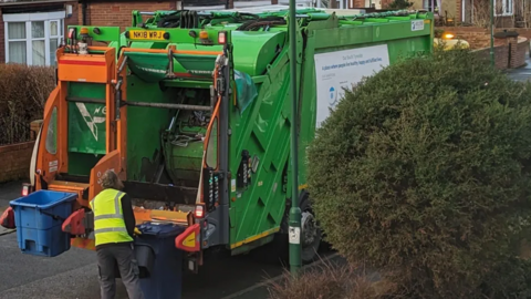 Man ready to load the contents of a wheelie bin into the back of a refuse vehicle