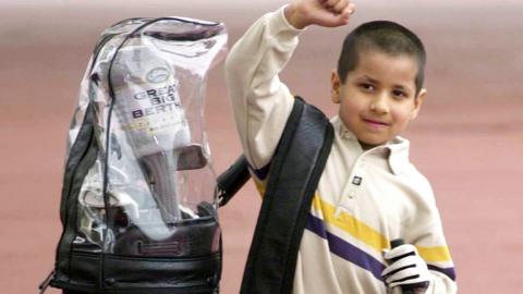 5-year-old Aaron Rai in 2000, raising his right arm, standing next to a large golf bag