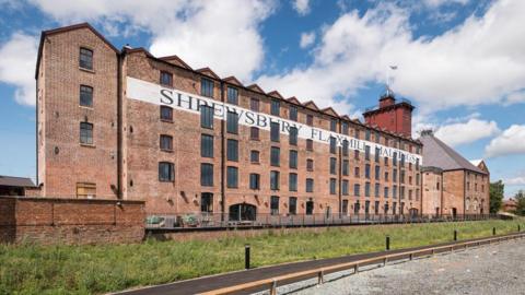 A large red brick building with five floors and dozens of windows and a red tower on the top