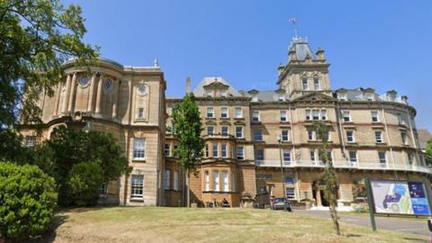 Bournemouth Town Hall - a large, grand, sandstone building with five floors incorporating French, Italianate and classical styles with pillars, bay windows and tall sash windows. Near the centre is a tower with a grey pointed roof topped with four corner turrets and a flagpole in the centre