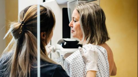 A nurse provides assistance to a patient undergoing a mammogram in a medical facility.