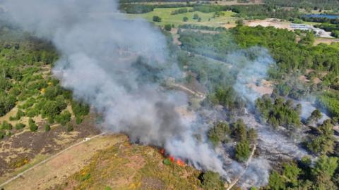 White and grey smoke rising over the countryside. The smoke comes from flames and charred ground.