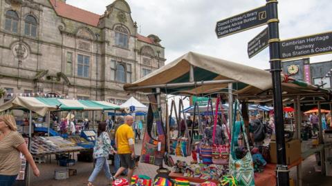 Oswestry's Guildhall, a three-storey building, is in the background. Market stalls and some people are in the foreground.