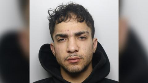 A mugshot of Marius Mihai. He has short curly black hair and dark facial hair. He is wearing a black hooded top.