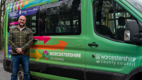 Councillor Karl Perks , a man in blue jeans and a cheque shirt is standing next to a green bus with the words, 'Worcestershire on demand' across the side.