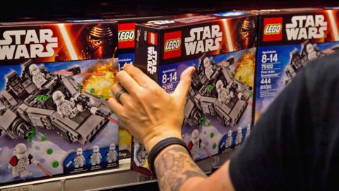 A man with a tattooed arm takes a packaged box of Star Wars lego off a shelf