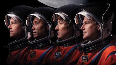 The Artemis II astronauts shown in a line with their space suits and helmets on.