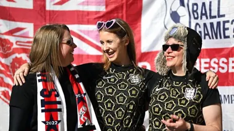Three female fans in front of an England flag