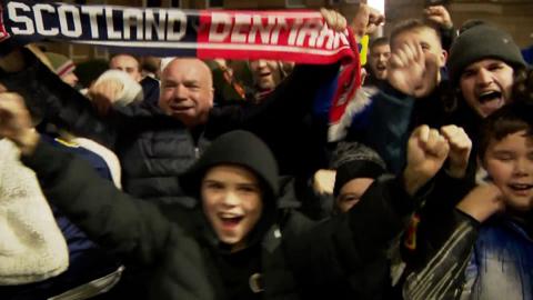 Group of cheering fans with a scarf raised reading "Scotland/Denmark"