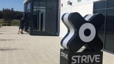 A picture of the Strive logo outside of a building. There is a glass entrance with tinted windows.