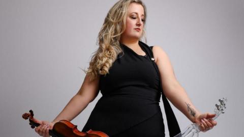 Woman holding violins in either hand wearing a black dress.
