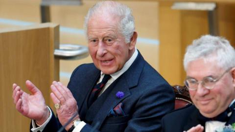 King Charles applauds in the chamber while sitting next to the presiding officer of the Scottish Parliament