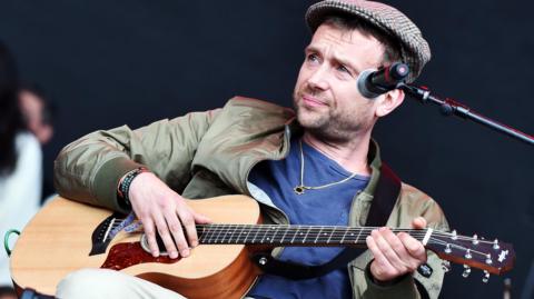 Damon Albarn playing an acoustic guitar