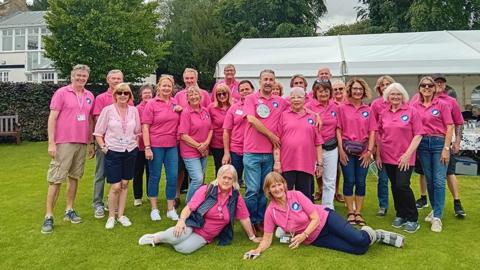 Volunteers from Pocklington Rugby in the Community wearing pink polo shirts pose on the grass in front of a large, white tent