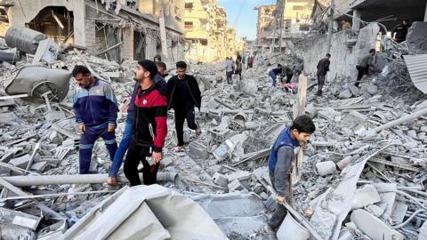 Palestinians search for survivors among a mess of rubble in a street after an Israeli air strike in Beit Lahia, northern Gaza (17 November 2024)