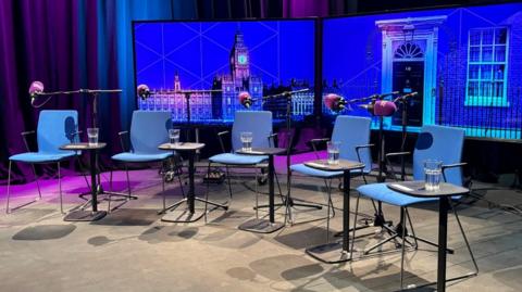 Five empty blue chairs with microphones