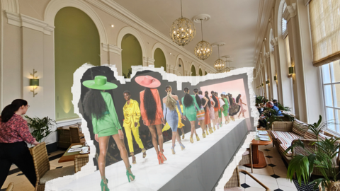 People working on the sustainable fashion show at Blenheim Palace. The runway showcases a concept image of fashion models in colourful outfits on a catwalk.