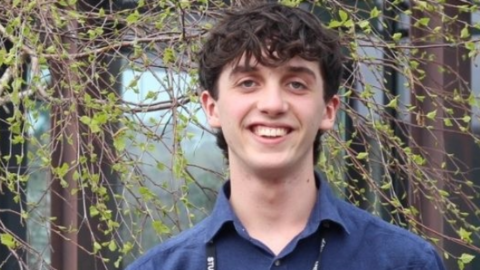 Lucas smiling at the camera with a tree behind him. He's wearing a blue shirt. 
