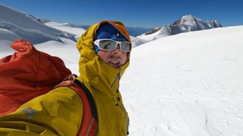 Ondrej Huserka dressed in yellow and wearing sunglasses, standing in snow-covered mountain landscape