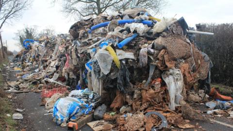 A huge pile of illegally dumped waste material, which appears to include housebuilding materials and tubing and various other items.