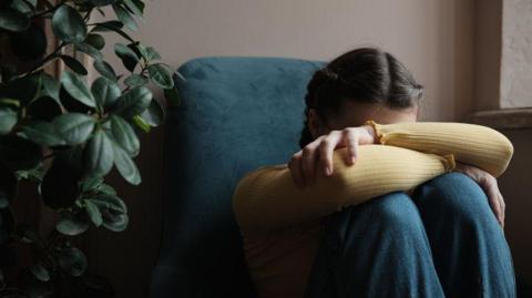 A young girl with her knees up, hiding her face. 