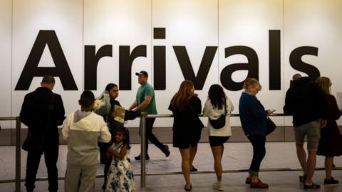 People wait to greet friends and relatives in front of a huge sign reading "Arrivals" at Heathrow Airport, Terminal 4, London.