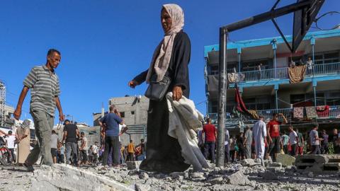 People walk over rubble next to a basketball court outside the al-Jaouni school in Nuseirat refugee camp following Israeli bombing on 11 September