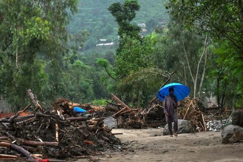 A villager holding an umbrella makes his way through the debris at the site of a flash flood in the Buner district of Pakistan's Khyber Pakhtunkhwa province.