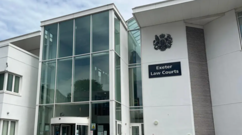 Modern white courthouse building with a large glass entrance and a sign reading “Exeter Law Courts” on the front exterior wall.