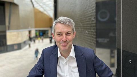 Will Forster, wearing a blue jacket and a white shirt, poses for a picture in the main foyer of the British Museum in London.
