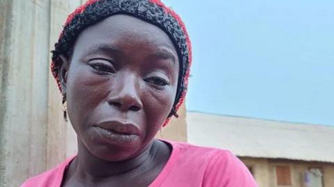 Nigerian woman Aisha Mohammed who lost three daughters in a boat disaster wearing a pink T-shirt and a hat, looking sad
