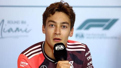 George Russell holds a microphone 