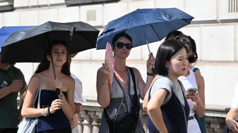 People using umbrellas and handheld fans for shade during hot weather in the UK 