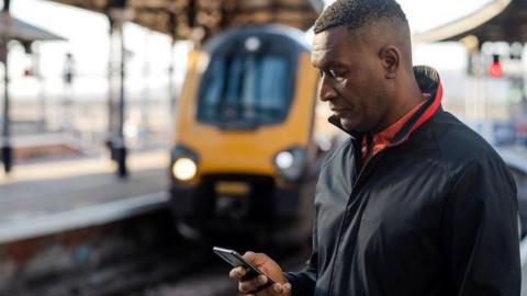 A man standing on a train platform looks at his mobile phone