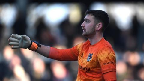 Jackson Smith pointing with his right hand in a match for Grimsby last month, dressed in an orange goalkeeper kit 