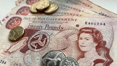 Red and beige £20 notes on a table with four gold round £1 and silver 50p and 10p coins on top of them.