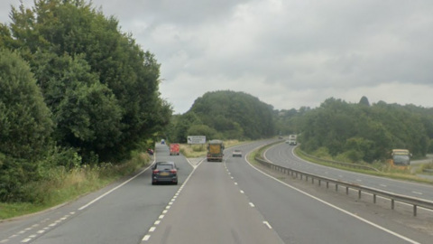 Google image of the A38 near the B3372 off slip. A car is turning off at the junction. A lorry continues along the dual carriageway. A central reservation separates the carriages.
