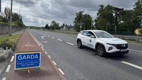 A blue garda sign and white garda car on the road
