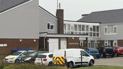 A grey and red brick block of flats. There are cars outside.